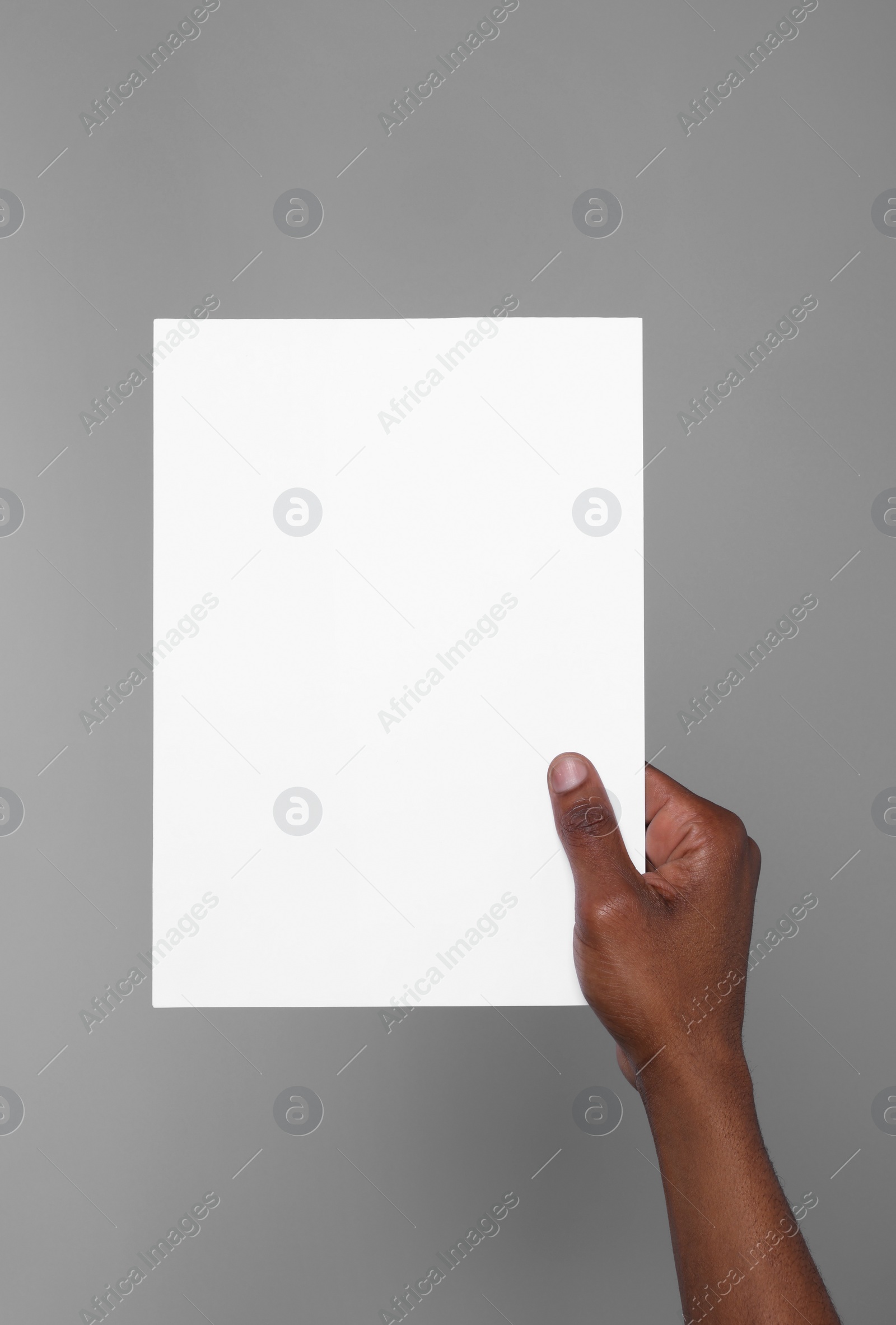 Photo of African American man holding sheet of paper on grey background, closeup. Mockup for design