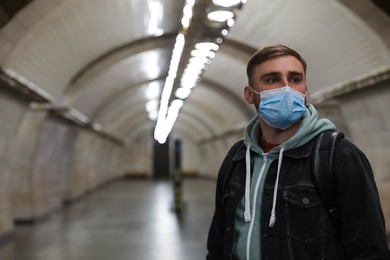 Young man in protective mask at subway station, space for text. Public transport