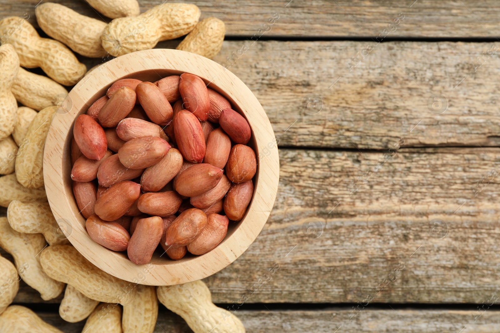 Photo of Fresh unpeeled peanuts in bowl on wooden table, top view. Space for text