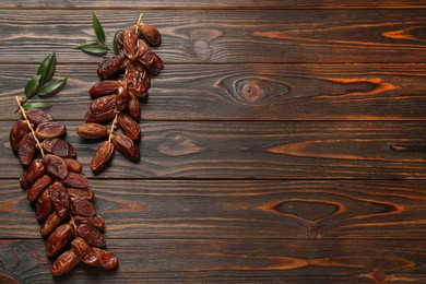 Photo of Branches with sweet dried dates and green leaves on wooden table, flat lay. Space for text