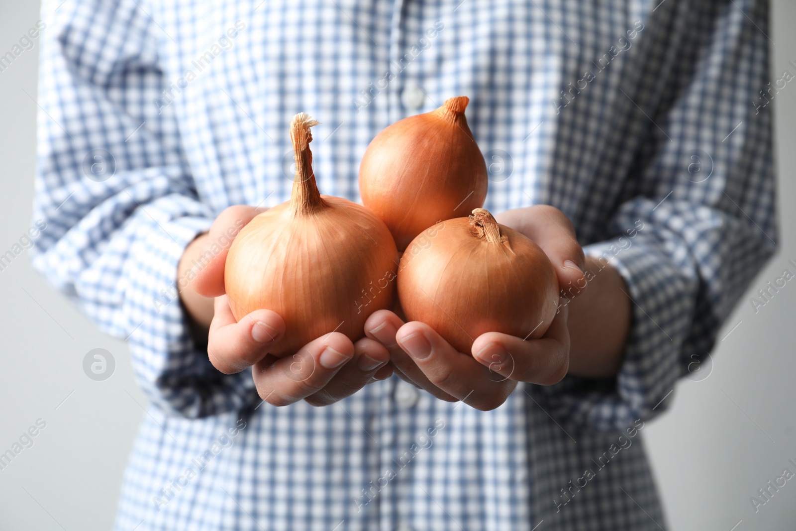 Photo of Woman holding raw yellow onion bulbs on grey background, closeup