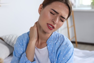 Photo of Woman suffering from neck pain in bedroom