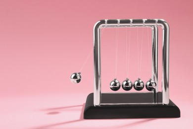 Photo of Newton's cradle on pink background, space for text. Physics law of energy conservation