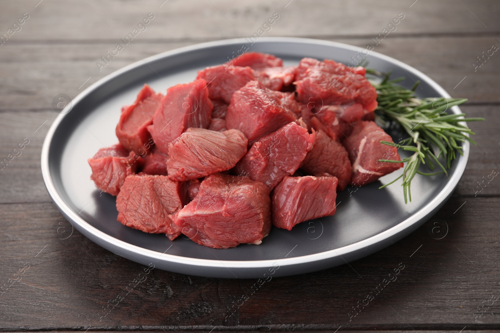 Photo of Pieces of raw beef meat with rosemary on wooden table, closeup