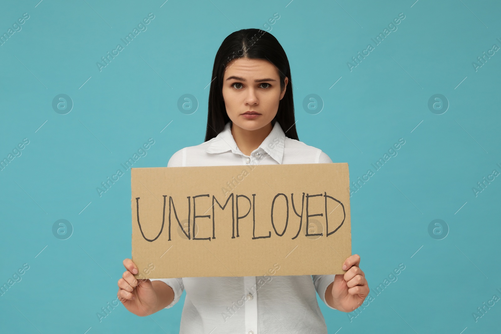 Photo of Unhappy woman holding sign with word Unemployed on light blue background