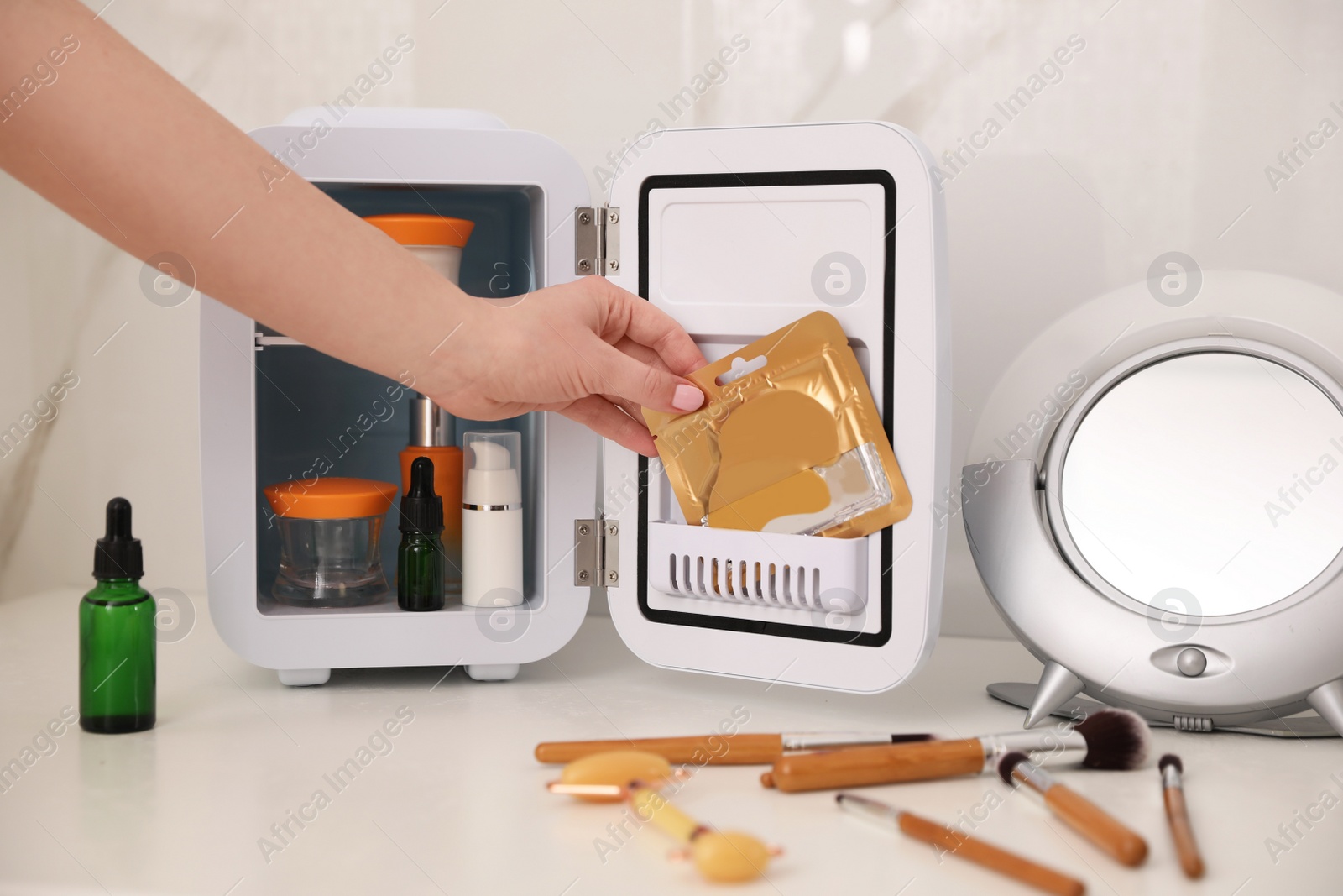 Photo of Woman taking eye patches out of cosmetic refrigerator indoors, closeup