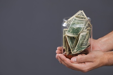 Man holding donation jar with money on grey background, closeup. Space for text