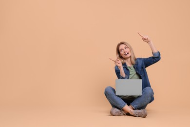 Happy woman with laptop pointing at something on beige background. Space for text