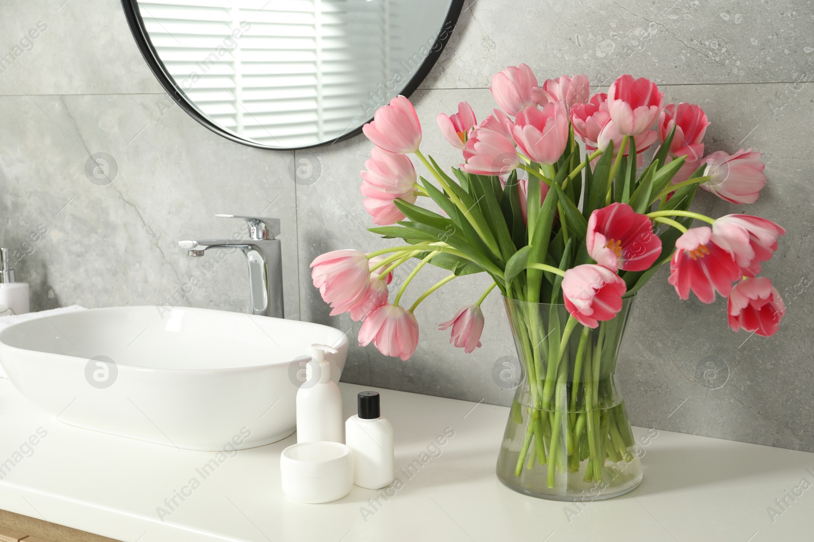 Photo of Vase with beautiful pink tulips and toiletries near sink in bathroom