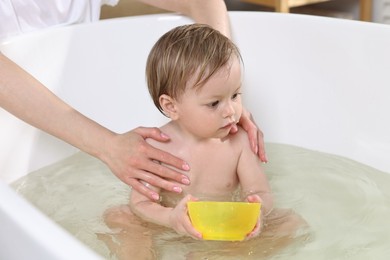 Mother bathing her cute little baby in tub at home