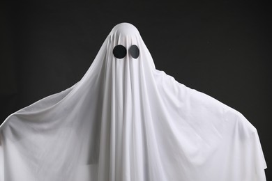 Creepy ghost. Person covered with white sheet on black background