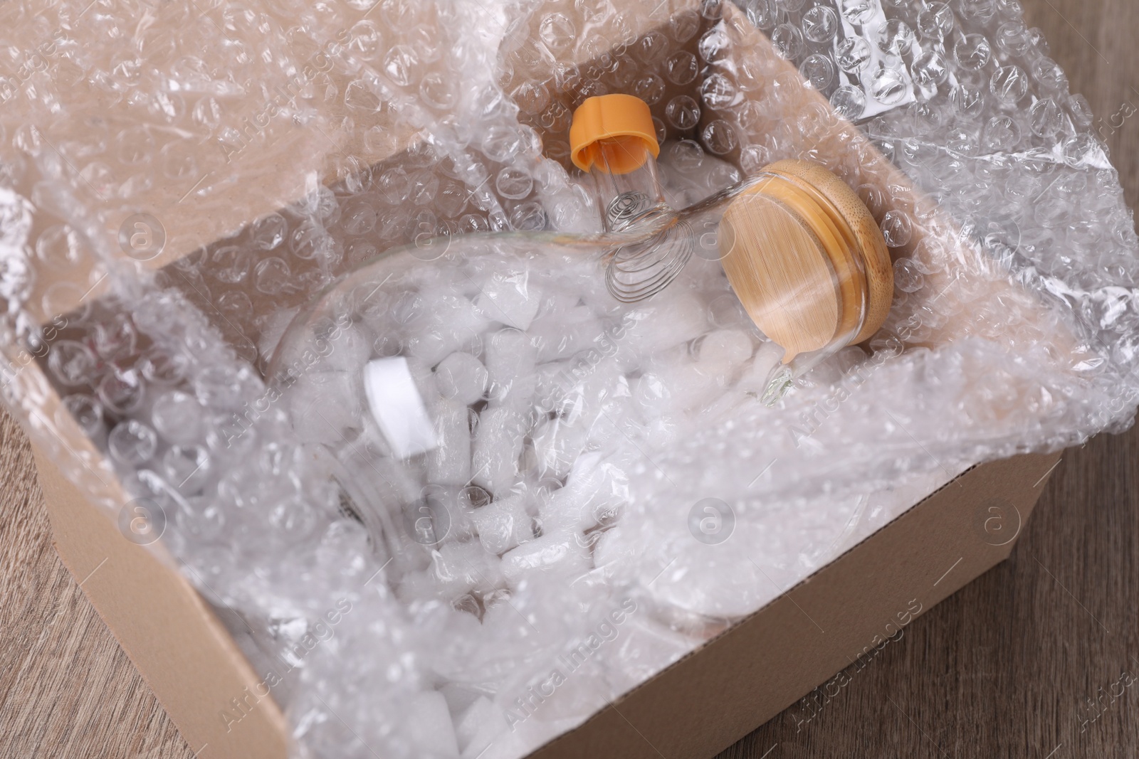 Photo of Flask with bubble wrap and packaging foam in cardboard box on wooden table, closeup