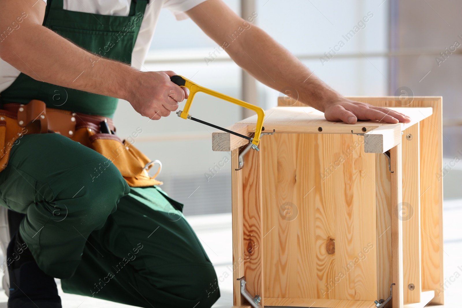 Photo of Carpenter in uniform making furniture indoors, closeup. Professional construction tools