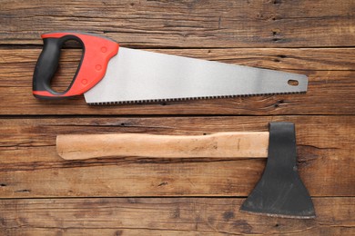 Photo of Saw with colorful handle and axe on wooden background, flat lay