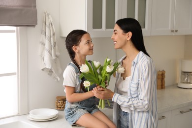 Photo of Little daughter congratulating her mom in kitchen at home. Happy Mother's Day