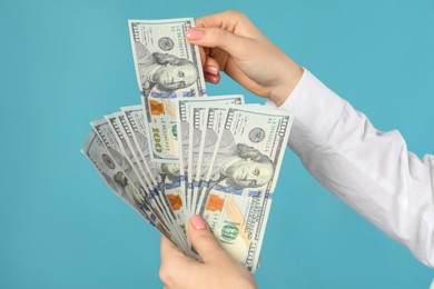 Woman holding dollar banknotes on turquoise background, closeup. Money exchange concept