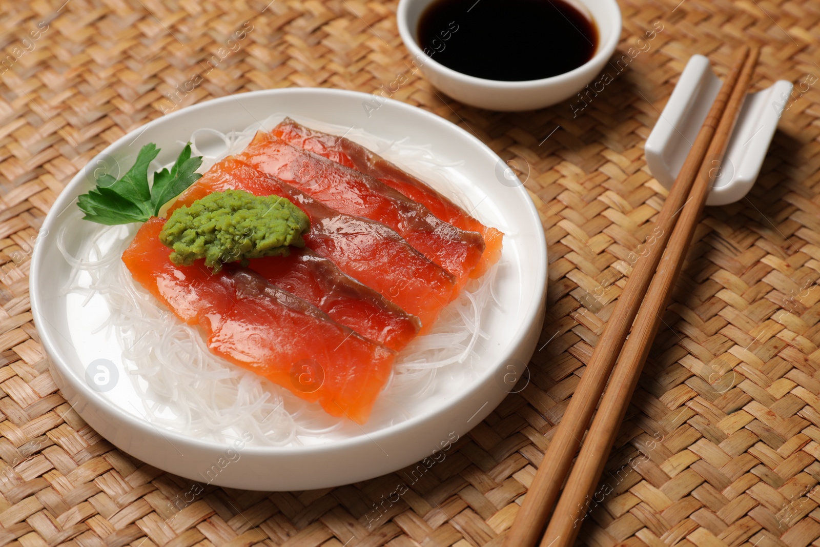 Photo of Sashimi set (raw salmon slices) served with funchosa, parsley, vasabi and soy sauce on wicker surface