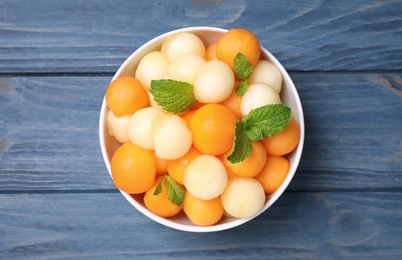 Melon balls and mint in bowl on blue wooden table, top view