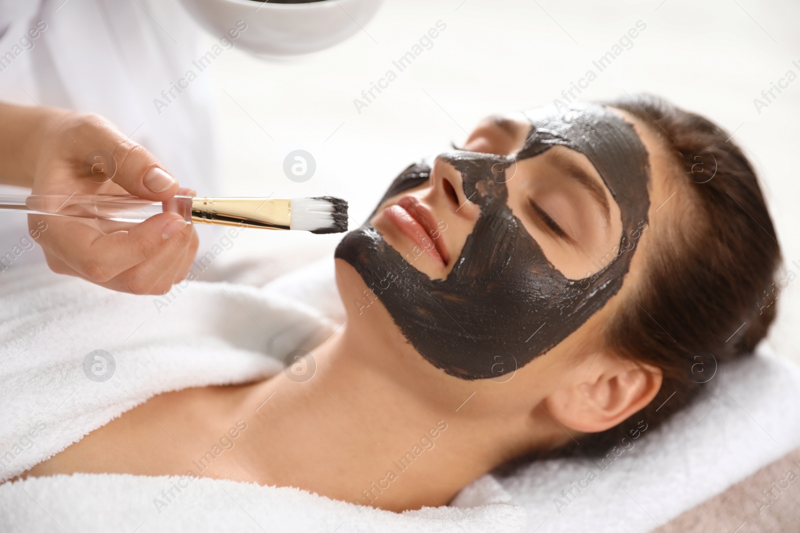 Photo of Cosmetologist applying black mask onto woman's face in spa salon