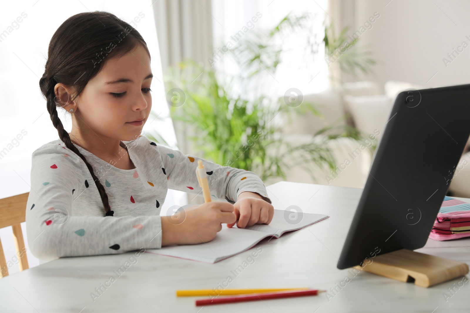 Photo of Little girl doing homework with modern tablet at home