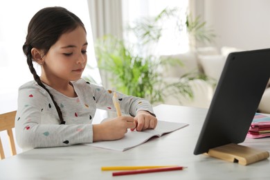 Photo of Little girl doing homework with modern tablet at home