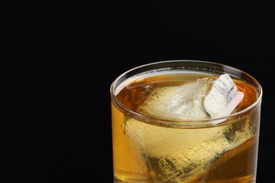 Photo of Tasty whiskey and ice in glass on black background, closeup. Space for text