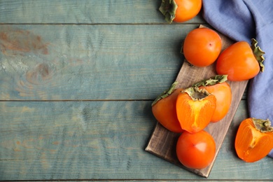 Photo of Tasty ripe persimmons on light blue wooden table, flat lay. Space for text