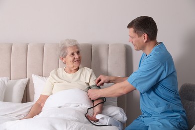 Caregiver measuring blood pressure of senior woman in bedroom. Home health care service