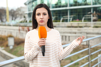 Young female journalist with microphone working on city street