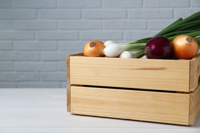 Photo of Crate with different kinds of onions on white wooden table, closeup. Space for text