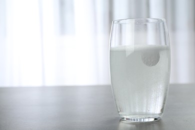 Photo of Glass with effervescent tablet on grey table indoors, space for text. Medical care