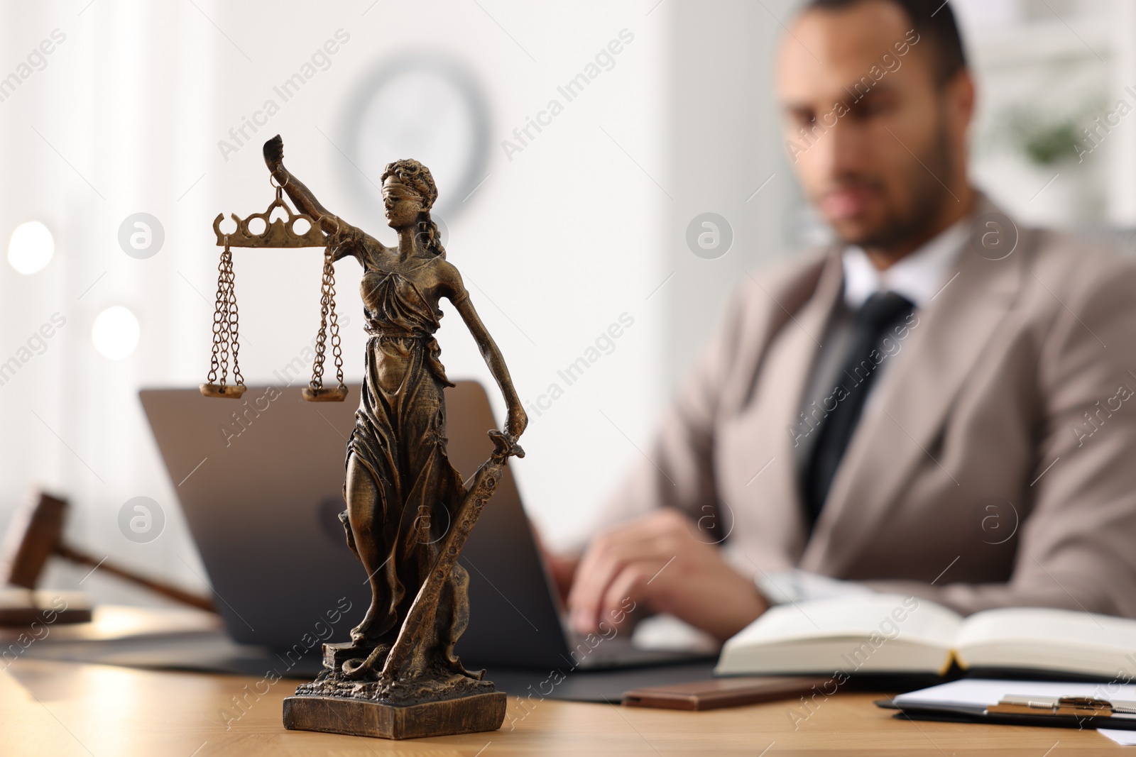 Photo of Lawyer working with laptop at table in office, focus on statue of Lady Justice