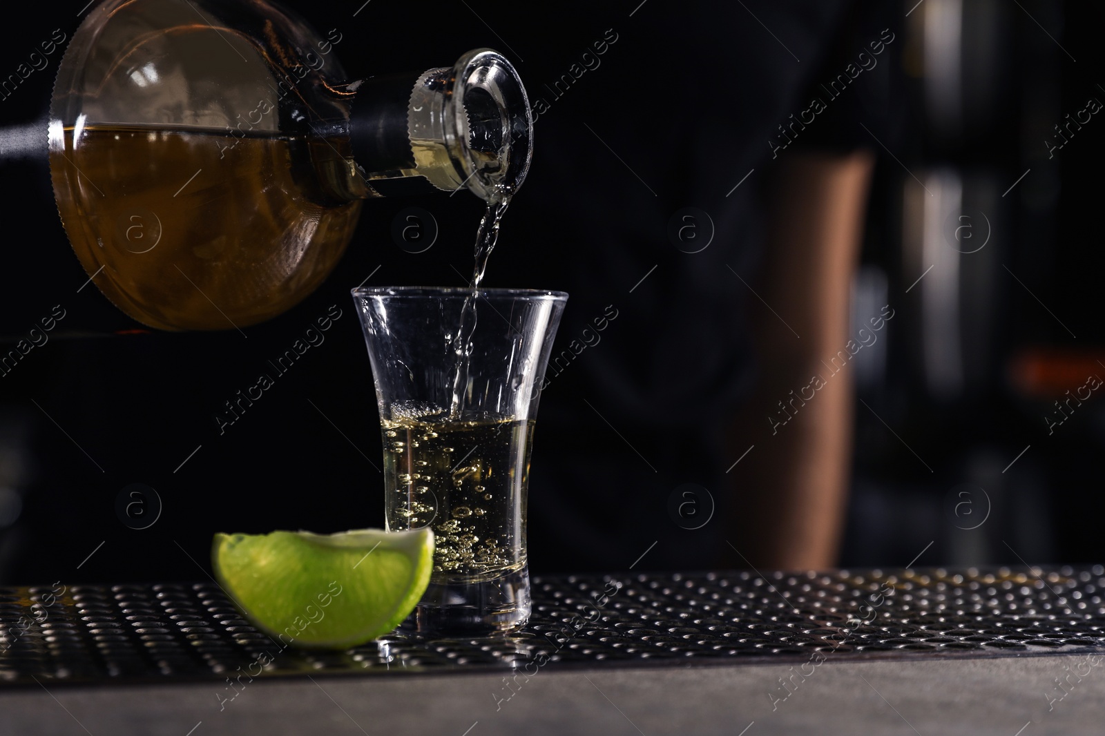 Photo of Bartender pouring Mexican Tequila into shot glass on bar counter, closeup. Space for text