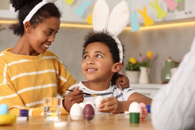 Photo of Happy African American mother and her cute son with Easter eggs at table in kitchen