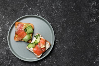 Photo of Tasty toasts with salmon, cream cheese and cucumber on black table, top view. Space for text