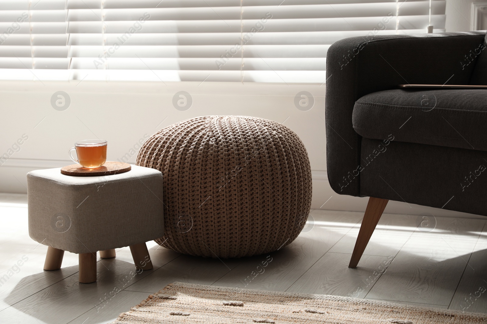 Photo of Tray with cup of tea on stylish ottoman and comfortable pouf in room