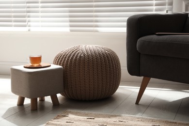 Tray with cup of tea on stylish ottoman and comfortable pouf in room