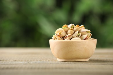 Tasty pistachios in bowl on wooden table against blurred background, closeup. Space for text