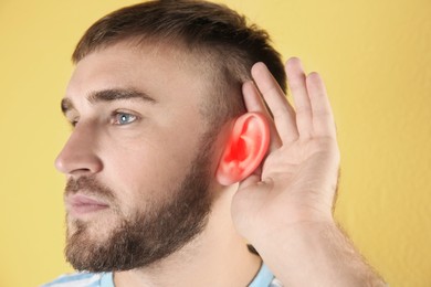 Image of Young man with hearing problem on yellow background
