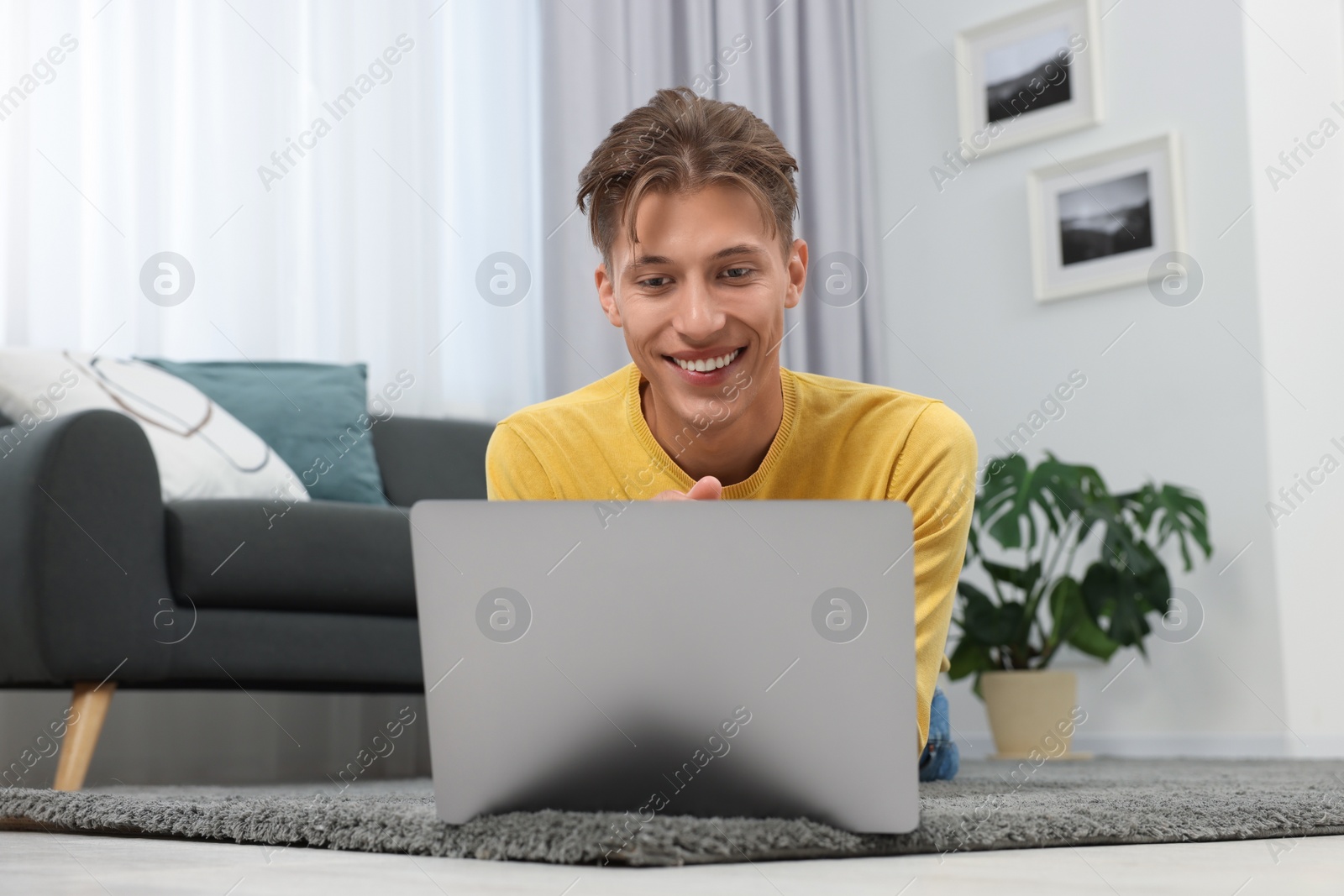 Photo of Happy young man having video chat via laptop on carpet indoors