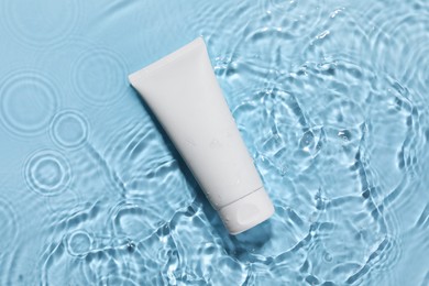 Tube of face cleansing product in water against light blue background, top view