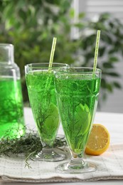 Photo of Glasses of homemade refreshing tarragon drink, sprigs and lemon on table