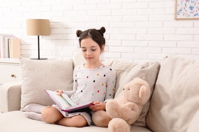 Photo of Little girl reading book on sofa at home