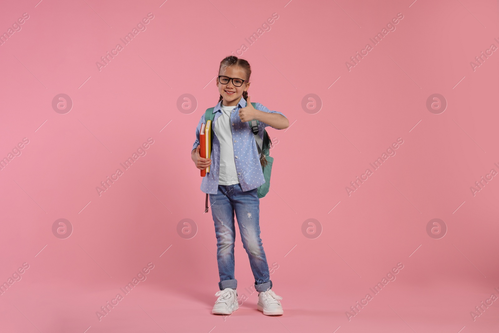 Photo of Happy schoolgirl in glasses with backpack and books on pink background