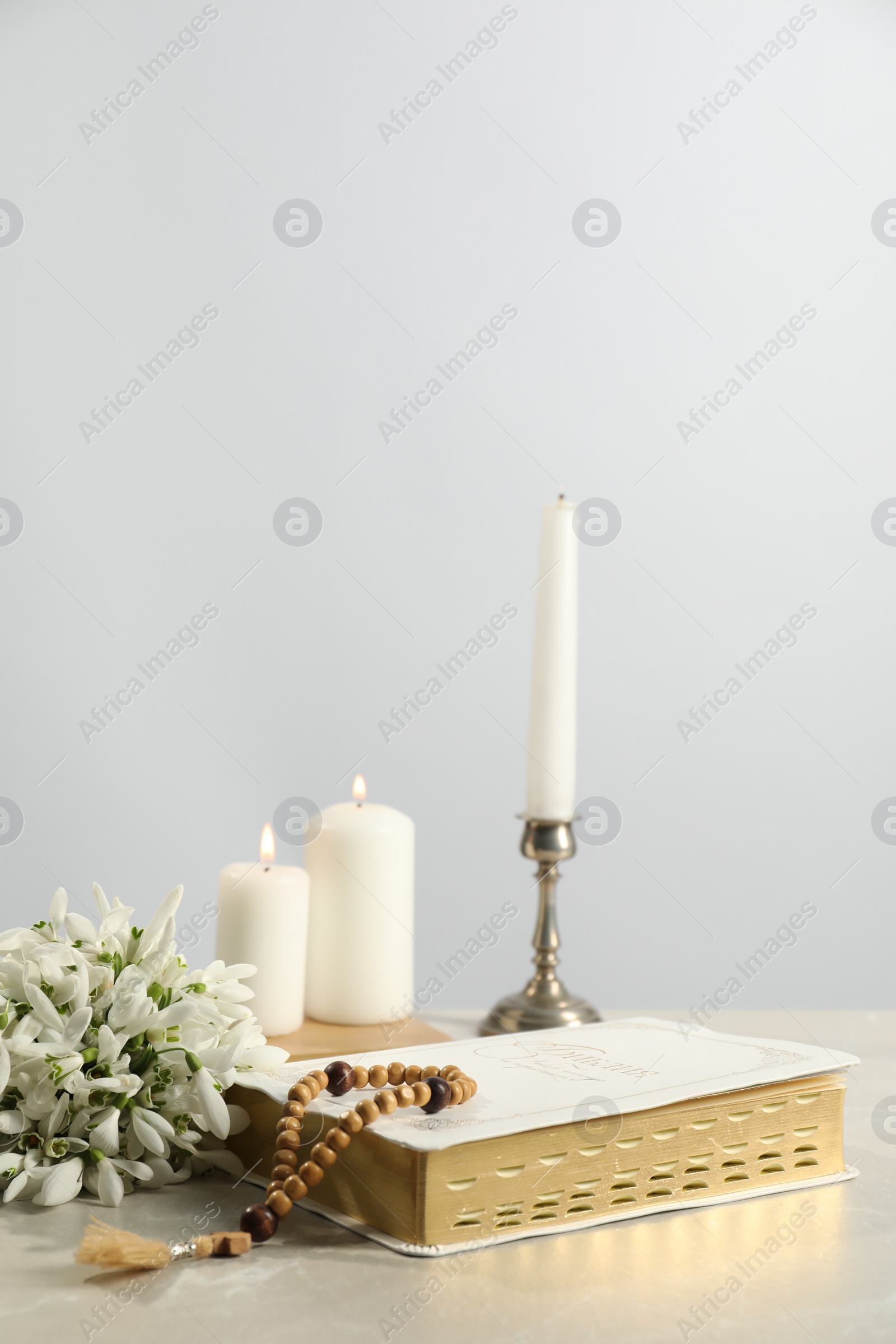 Photo of Church candles, wooden cross, rosary beads, Bible and flowers on light table