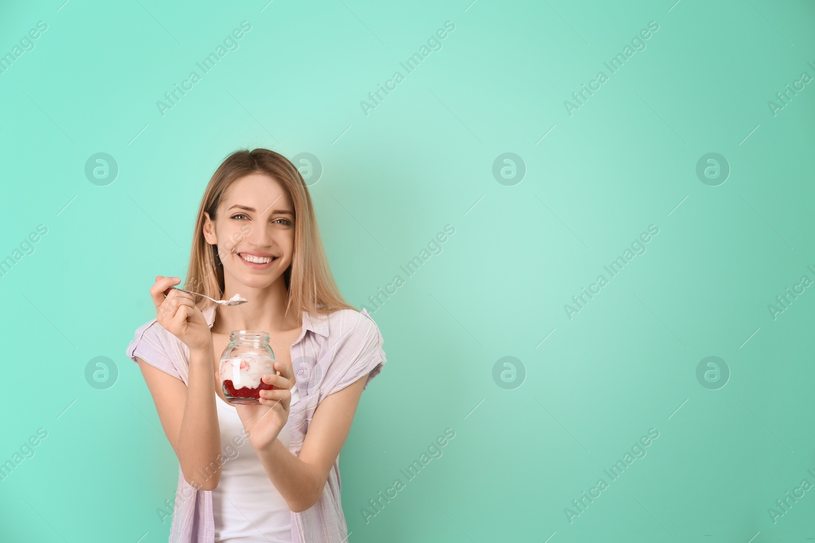 Photo of Young attractive woman eating tasty yogurt on color background