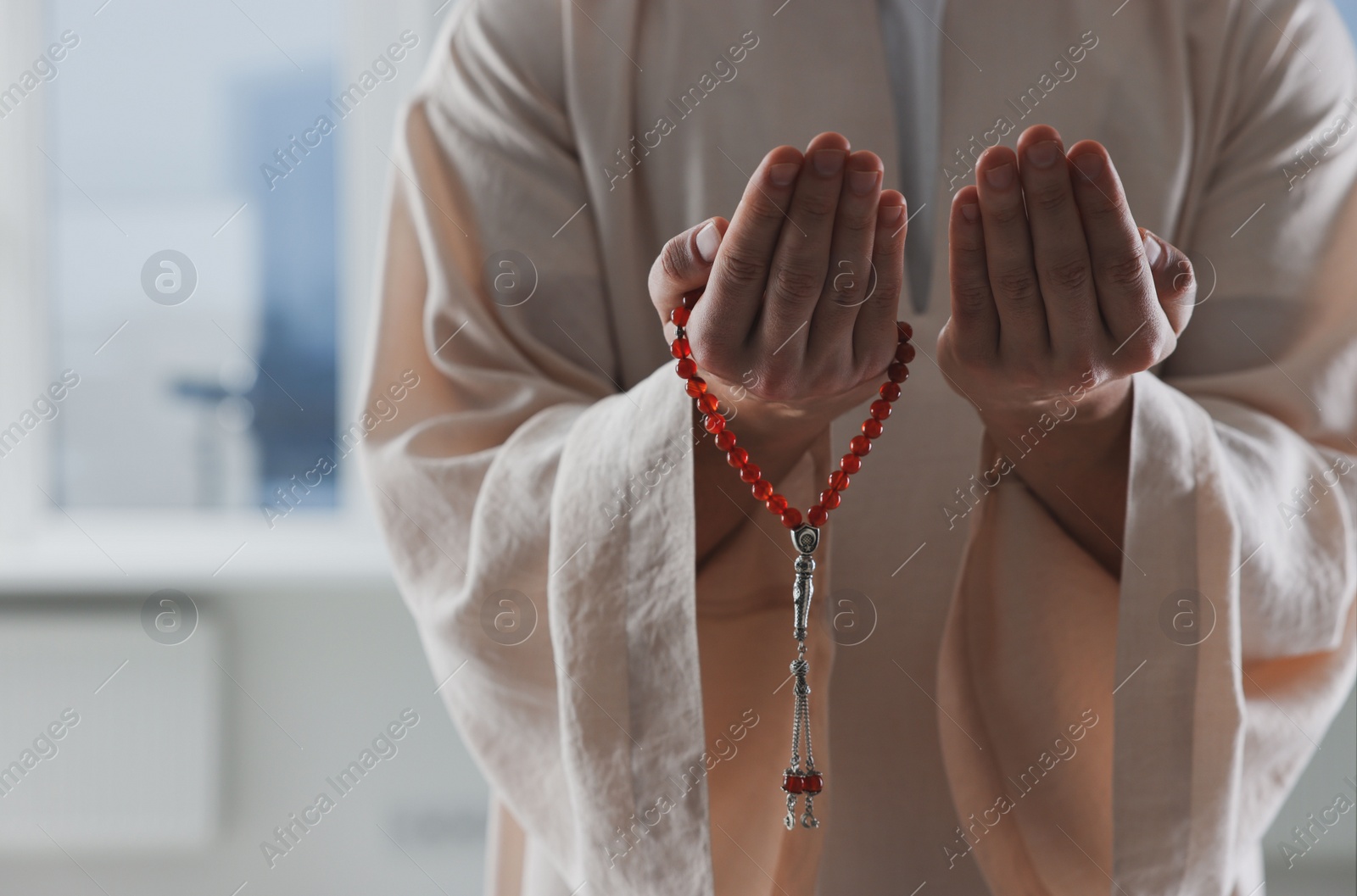 Photo of Muslim man with misbaha praying near window indoors, closeup. Space for text