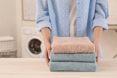 Photo of Woman with folded clean terry towels at table in laundry room, closeup