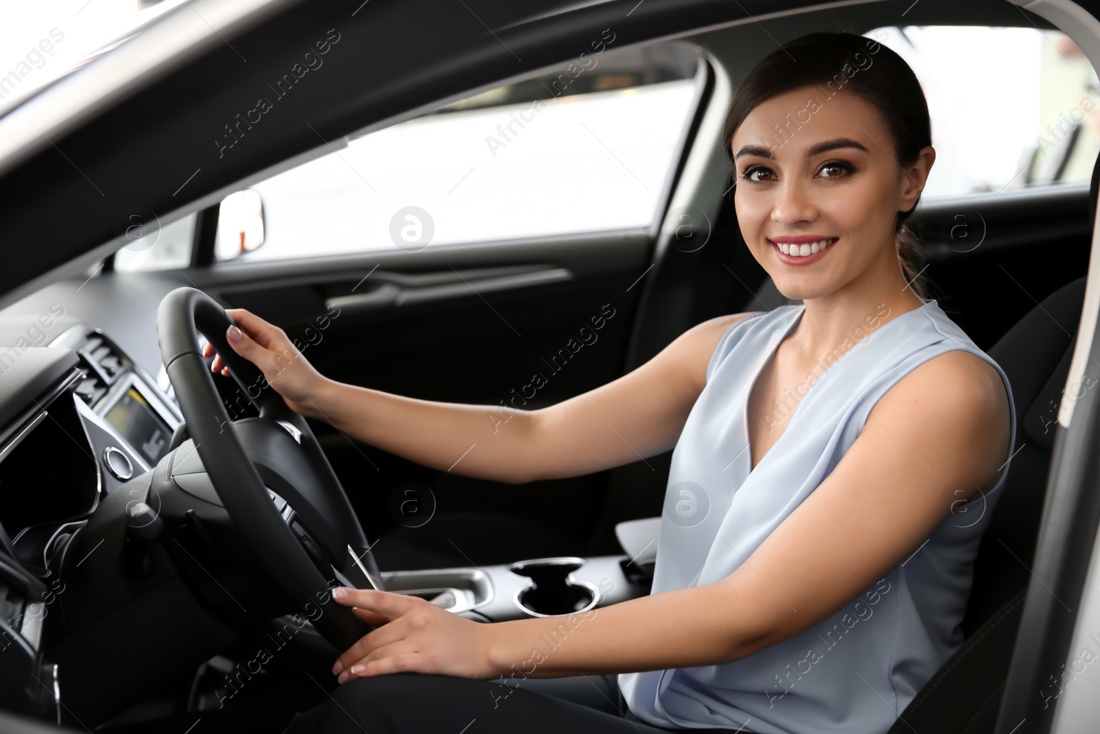 Photo of Young woman sitting in driver's seat of new car at salon