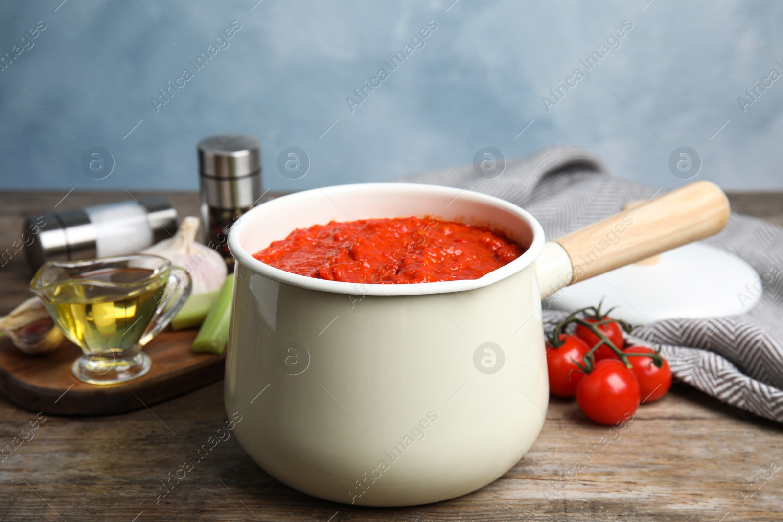 Photo of Pan of tomato sauce on wooden table against blue background